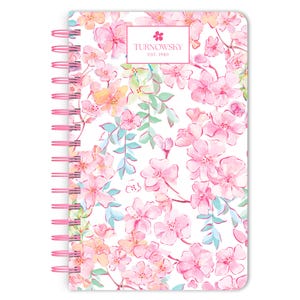 May include: A pink spiral bound notebook with a white background and a floral pattern of pink, yellow, and blue flowers. The notebook has the text "TURNOWSKY EST. 1940" on the front cover.