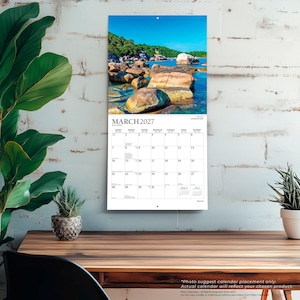 May include: A wall calendar for March 2027 featuring a landscape photograph of large brown rocks in clear blue water under a bright sky. The calendar grid displays the month, days of the week, and dates in black text on a white background.