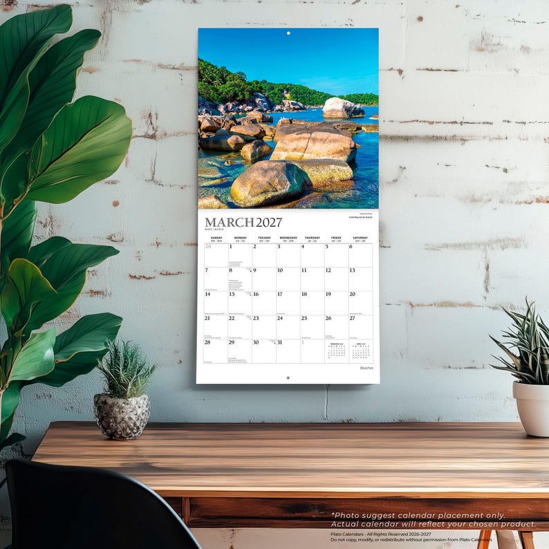 May include: A wall calendar for March 2027 featuring a landscape photograph of large brown rocks in clear blue water under a bright sky. The calendar grid displays the month, days of the week, and dates in black text on a white background.