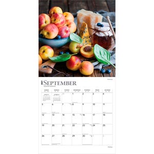Puede incluir: Un calendario de pared para septiembre de 2027 con una imagen de melocotones frescos en un cuenco azul, un tarro de mermelada, un trozo de queso y hojas verdes. La parte inferior muestra una cuadr&iacute;cula para el mes con fechas del 1 al 30.
