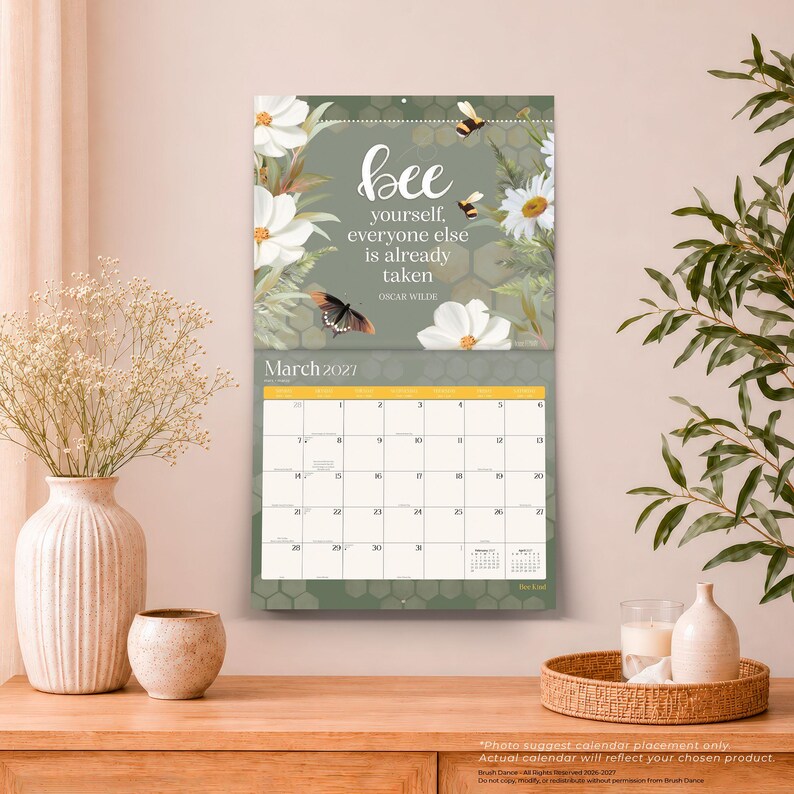 May include: A wall calendar for March 2027 featuring a sage green background with white flowers, a butterfly, and bees. The text reads: bee yourself, everyone else is already taken, Oscar Wilde. The grid displays dates from 1 to 31 in a white layout.