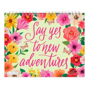May include: A 2027 desk calendar with a spiral binding at the top. The cover features a light yellow background with a vibrant floral border of pink, red, yellow, and white flowers and butterflies. The text reads: Say yes to new adventures.