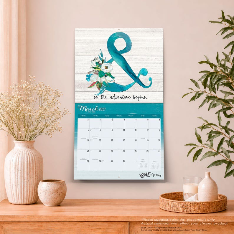 May include: A wall calendar for March 2027 featuring a white wood-plank background with a large teal ampersand symbol decorated with white and teal flowers. The text reads "so the adventure begins." and "LOVE by Fancy" at the bottom.