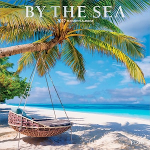 May include: A 2027 16-month calendar titled BY THE SEA featuring a photograph of a brown woven hanging chair suspended from a palm tree on a white sandy beach with turquoise ocean water under a bright blue sky with scattered white clouds.