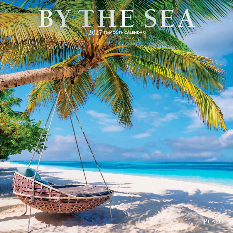 May include: A 2027 16-month calendar titled BY THE SEA featuring a photograph of a brown woven hanging chair suspended from a palm tree on a white sandy beach with turquoise ocean water under a bright blue sky with scattered white clouds.