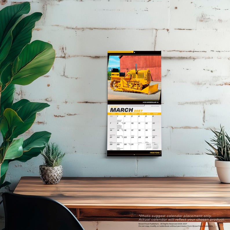 May include: A wall calendar for March 2027 featuring a photograph of a yellow Caterpillar 15 tractor on the top half. The calendar grid displays the month, year, and dates clearly in black text on a white background with yellow accents.