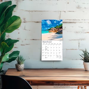 May include: A wall calendar for March 2027 featuring a photograph of a tropical beach with white sand, turquoise water, and large boulders under a blue sky. The calendar grid displays the days of the month with black text on a white background.