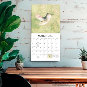 K&ouml;nnte beinhalten: Ein Wandkalender f&uuml;r M&auml;rz 2027 mit einer Aquarellillustration eines Kolibris vor einem sanften gr&uuml;nen Hintergrund. Der Text "He restores my soul" steht in wei&szlig;er Schreibschrift &uuml;ber dem Vogel. Das Kalenderraster zeigt die Daten des Monats.