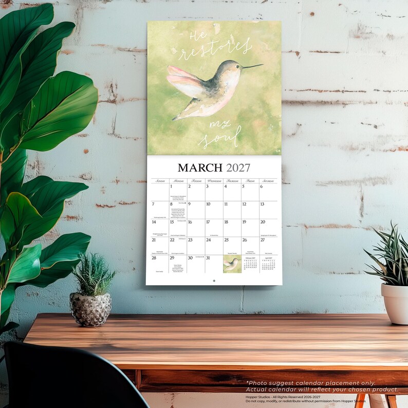 K&ouml;nnte beinhalten: Ein Wandkalender f&uuml;r M&auml;rz 2027 mit einer Aquarellillustration eines Kolibris vor einem sanften gr&uuml;nen Hintergrund. Der Text "He restores my soul" steht in wei&szlig;er Schreibschrift &uuml;ber dem Vogel. Das Kalenderraster zeigt die Daten des Monats.
