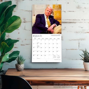 Puede incluir: Un calendario de pared que muestra el mes de marzo, con una fotograf&iacute;a de un hombre con traje. El calendario tiene una cuadr&iacute;cula de fechas. La palabra "Marzo" est&aacute; en la parte superior. El calendario est&aacute; colgado en una pared de ladrillos blancos.