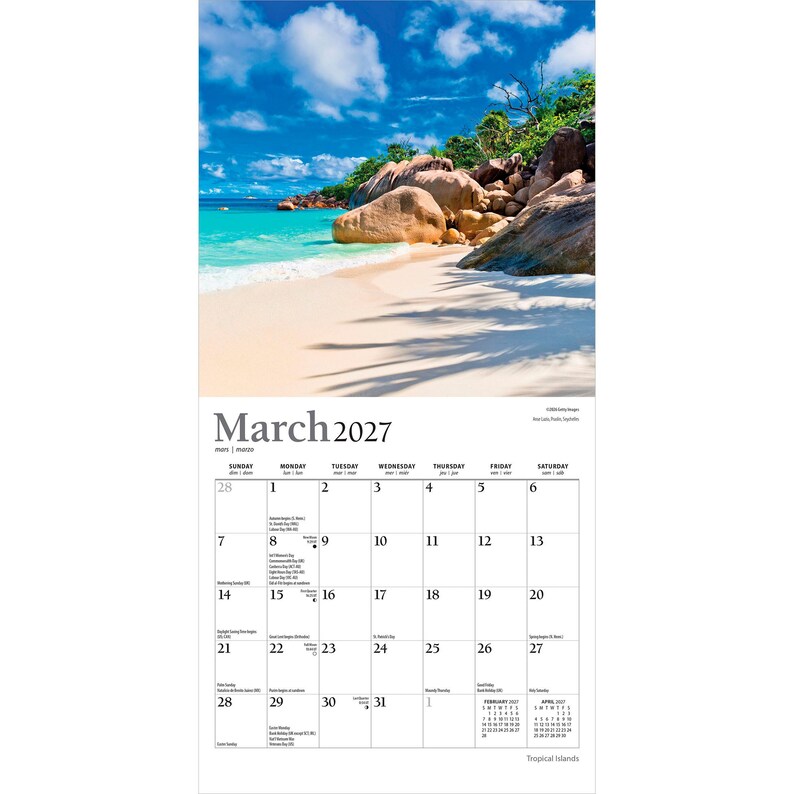 May include: A wall calendar for March 2027 featuring a photograph of a tropical beach with white sand, turquoise water, and large granite boulders under a blue sky with clouds. The calendar grid displays dates, days of the week, and holidays.