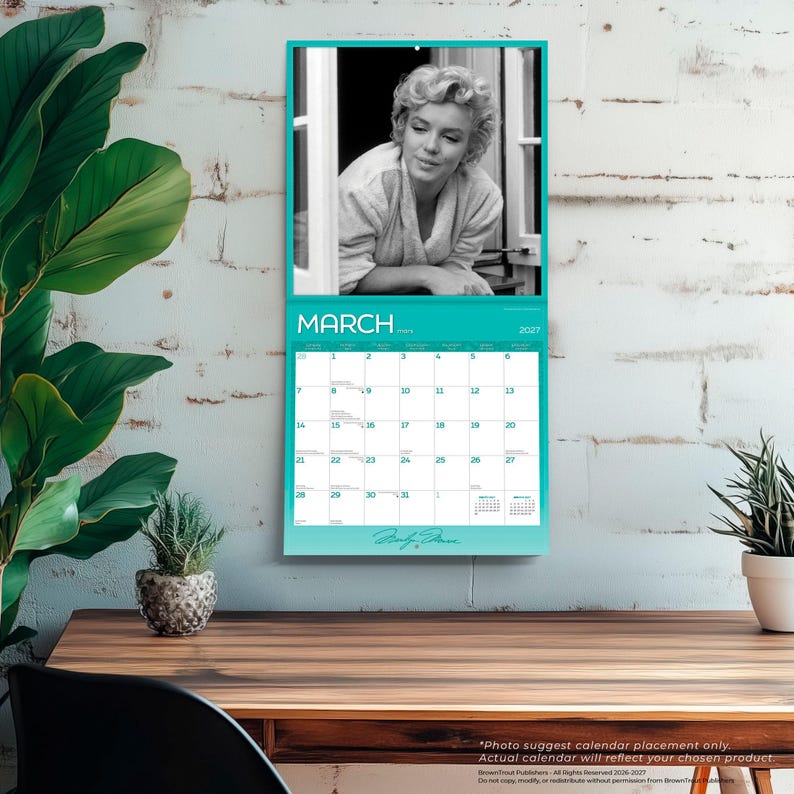 May include: A 2027 wall calendar for the month of March featuring a black and white photograph of Marilyn Monroe in a robe. The calendar grid is printed in white and teal with the text MARCH 2027 and a signature at the bottom of the page.