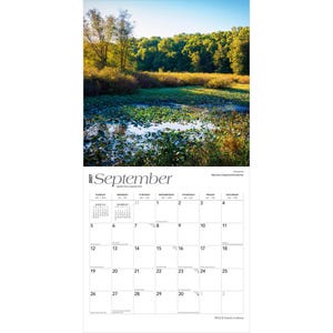 May include: A 2027 wall calendar for the month of September featuring a photograph of a sunlit marshland with green lily pads and dense trees. The calendar grid displays the days of the month with black text on a white background, including small reference calendars for August and October.