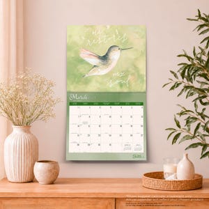 May include: A wall calendar for March 2027 featuring a watercolour illustration of a hummingbird against a soft green background. The text reads He restores my soul. The calendar grid displays the days of the month with a small preview of adjacent months.