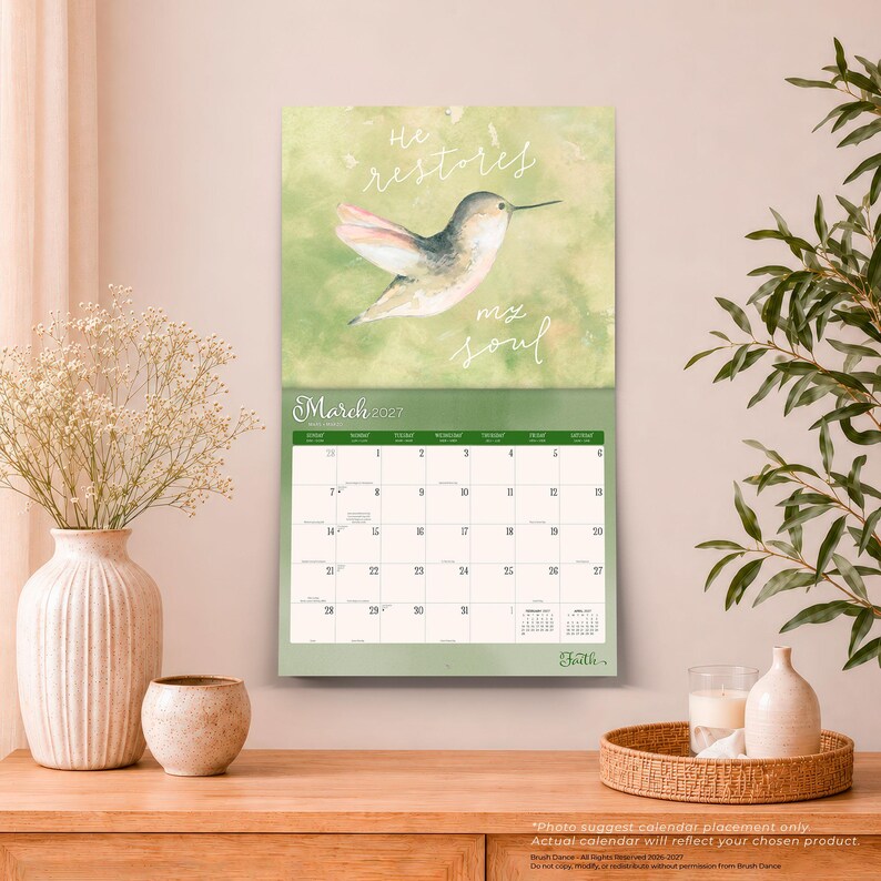 May include: A wall calendar for March 2027 featuring a watercolour illustration of a hummingbird against a soft green background. The text reads He restores my soul. The calendar grid displays the days of the month with a small preview of adjacent months.