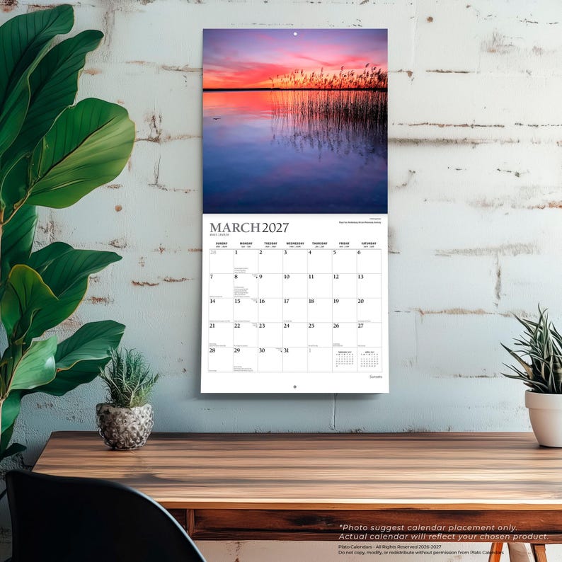 Pu&ograve; includere: Un calendario da parete per marzo 2027 con una fotografia di canne alte al bordo di un lago calmo durante un vivace tramonto rosa e arancione. La griglia del calendario mostra i giorni del mese con testo nero su uno sfondo bianco.