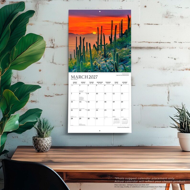 Peut inclure: Un calendrier mural pour mars 2027 pr&eacute;sentant une photographie d'un paysage d&eacute;sertique avec de grands cactus saguaro en silhouette sur un coucher de soleil orange et violet. La grille du calendrier affiche les jours en noir.