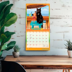 Pode incluir: Um calend&aacute;rio de parede para mar&ccedil;o de 2024 com uma fotografia de um gato preto sentado num banco azul brilhante ao lado de um boneco masculino com cal&ccedil;&otilde;es de banho vermelhos. O fundo mostra uma praia com um bar de madeira e um chap&eacute;u de palha.