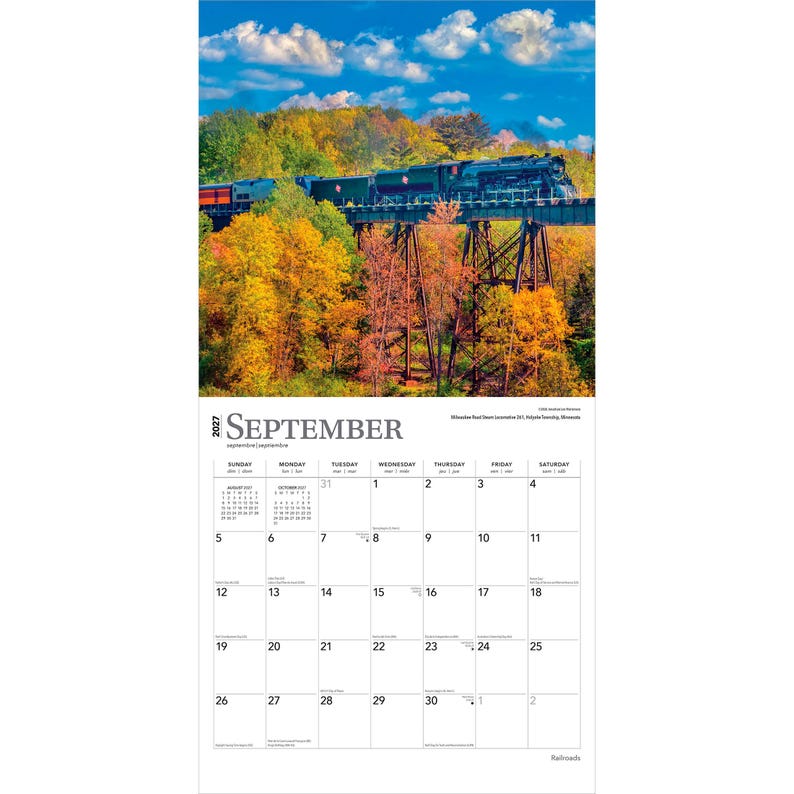 K&ouml;nnte beinhalten: Ein Wandkalender f&uuml;r September 2027 mit einer dunkelgr&uuml;nen Dampflokomotive, die &uuml;ber eine hohe Metall-Trestle-Br&uuml;cke f&auml;hrt, &uuml;ber einem Wald mit leuchtendem Herbstlaub unter einem blauen Himmel mit wei&szlig;en Wolken. Das Kalenderraster zeigt die Daten.
