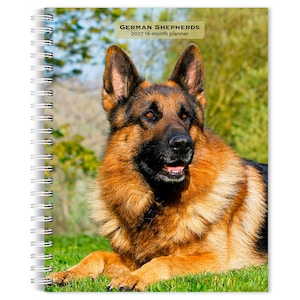 May include: A spiral-bound 2027 16-month planner featuring a photograph of a German Shepherd dog on the cover. The dog has black and tan fur, pointed ears, and is lying down. The text on the cover reads: GERMAN SHEPHERDS 2027 16-month planner.