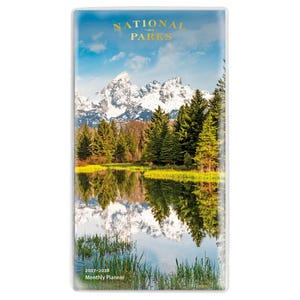 May include: A rectangular 2027-2028 monthly planner featuring a scenic cover image of snow-capped mountains, a dense forest of green pine trees, and a calm lake reflecting the landscape. The text NATIONAL PARKS is printed in gold at the top.