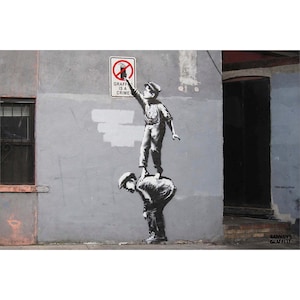May include: A black and white mural depicting two children, one standing on the shoulders of the other, reaching towards a sign that reads "Graffiti is a Crime." The artwork is on a gray wall.