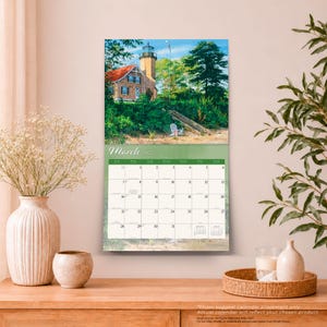 Peut inclure: Un calendrier mural pour mars 2025 illustr&eacute; par une peinture d'un phare en pierre au toit rouge entour&eacute; d'arbres et de feuillage verts. La grille du calendrier affiche les jours du mois avec des petits calendriers de r&eacute;f&eacute;rence pour f&eacute;vrier et avril.