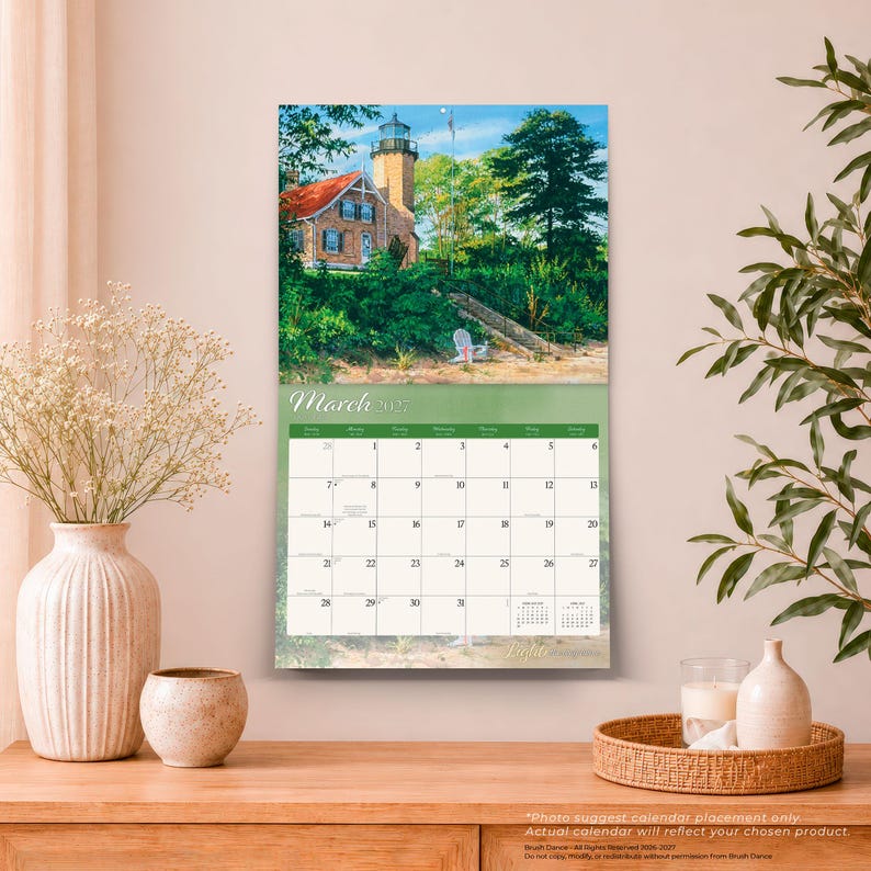 Peut inclure: Un calendrier mural pour mars 2025 illustr&eacute; par une peinture d'un phare en pierre au toit rouge entour&eacute; d'arbres et de feuillage verts. La grille du calendrier affiche les jours du mois avec des petits calendriers de r&eacute;f&eacute;rence pour f&eacute;vrier et avril.