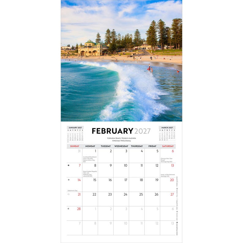 May include: A wall calendar page for February 2027 featuring a photograph of a turquoise ocean wave breaking near a sandy beach with a large building and tall pine trees in the background under a blue sky with light clouds.
