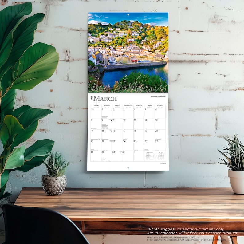 May include: A wall calendar for March 2027 featuring a photograph of a coastal village with white buildings, green hills, and a harbor with boats. The calendar grid displays the days of the month with the text March 2027 clearly visible at the top.