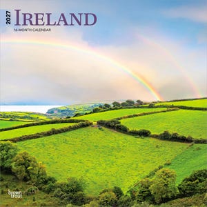 May include: A 2027 Ireland 16-month calendar featuring a landscape photograph of vibrant green rolling hills and fields under a double rainbow in a cloudy sky. The text 2027 IRELAND 16-MONTH CALENDAR is printed in dark purple at the top left corner.