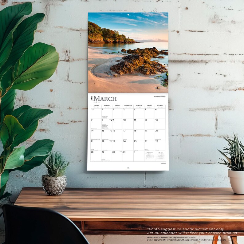 May include: A wall calendar for March 2025 featuring a scenic photograph of a sandy beach with rocky formations, calm water, and a treelined coastline under a blue sky. The calendar grid displays dates, days of the week, and small monthly views.