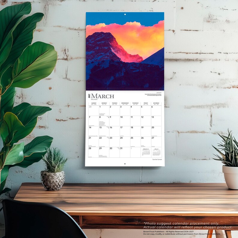 May include: A wall calendar for March 2023 featuring a landscape photograph of a mountain range at sunset with vibrant orange and pink clouds above dark blue peaks. The calendar grid displays the days of the month in a standard black and white layout.