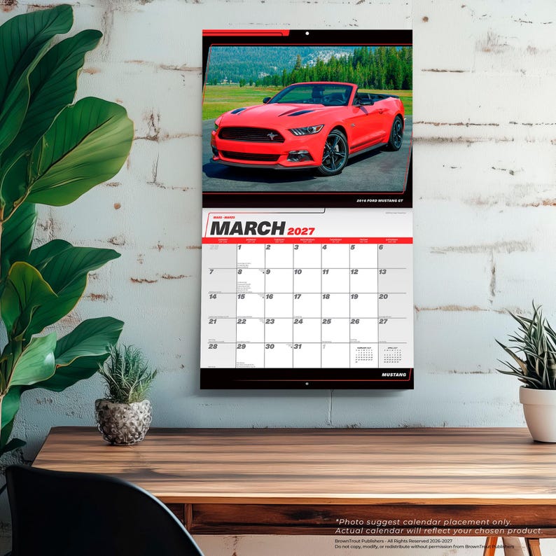 May include: A wall calendar for March 2027 featuring a photograph of a bright red Ford Mustang convertible parked on asphalt. The calendar grid displays the month, year, and dates in black text on a white background with red accents.