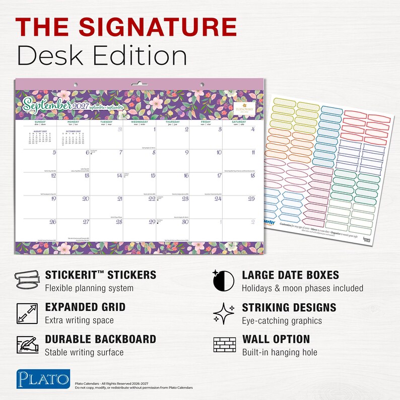 May include: A desk calendar titled THE SIGNATURE Desk Edition featuring a floral purple border and a grid for September 2027. It includes a sheet of colorful rectangular stickers, a hanging hole, and text detailing features like large date boxes and a durable backboard.