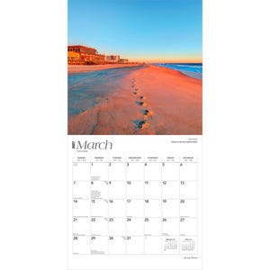 May include: A 2027 wall calendar for the month of March featuring a photograph of a sandy beach at sunset with footprints leading toward the ocean and a building in the distance. The calendar grid displays dates from March 1st through March 31st.