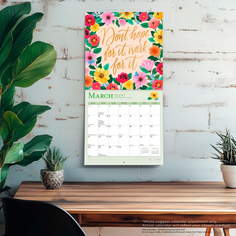 May include: A wall calendar for March 2027 featuring a floral border of pink, yellow, orange, and red flowers surrounding the gold cursive text Don't hope for it, work for it. The grid below displays the days of the month with a light green header.