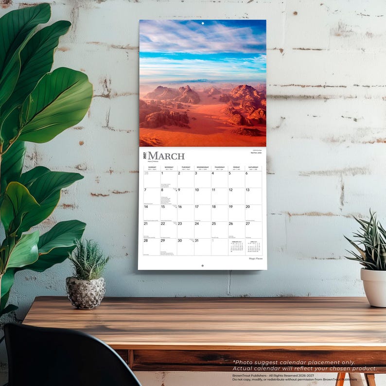 May include: A wall calendar for March 2027 featuring a landscape photograph of a desert with red sand dunes and rocky mountains under a blue sky. The calendar grid displays the days of the month with the text March 2027 clearly printed at the top.