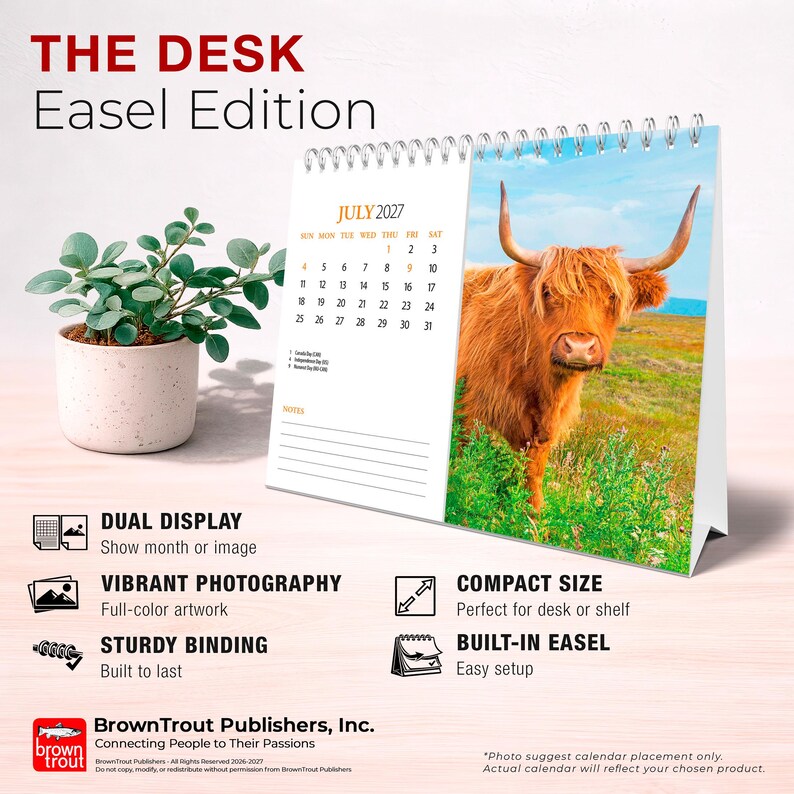 May include: A desk easel calendar titled THE DESK Easel Edition, featuring a spiral binding and a photograph of a Highland cow in a field. The calendar page shows July 2027 with a grid of dates, a notes section, and text describing product features.