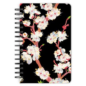 May include: A black spiral notebook with a floral design featuring white and pink flowers on a black background.