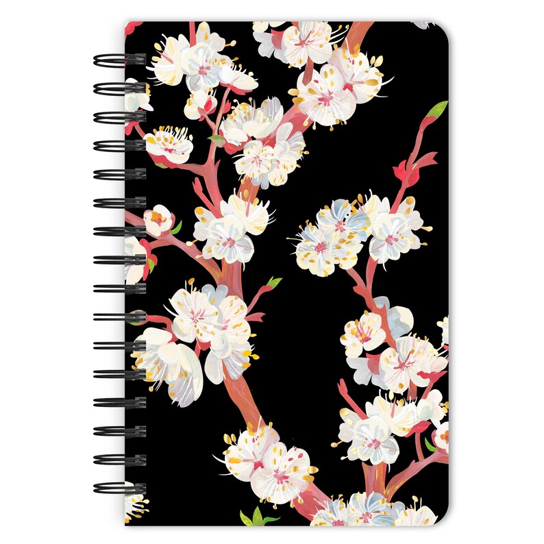 May include: A black spiral notebook with a floral design featuring white and pink flowers on a black background.