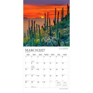 Peut inclure: Un calendrier mural pour mars 2027 pr&eacute;sentant une photographie d'un paysage d&eacute;sertique avec de grands cactus saguaro en silhouette sur un coucher de soleil orange et rouge vif. La grille du calendrier affiche les jours avec du texte noir.