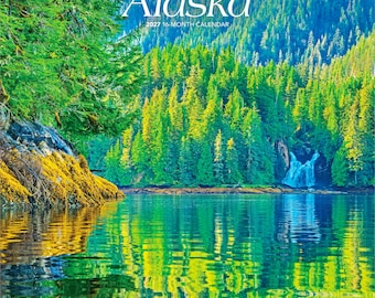 Puede incluir: Un calendario de pared de 16 meses para 2027 titulado Wild & Scenic Alaska con una fotografía de un lago tranquilo que refleja un denso bosque verde y una cascada. El texto dice Wild & Scenic Alaska 2027 16-Month Calendar con el logo Brown Trout.
