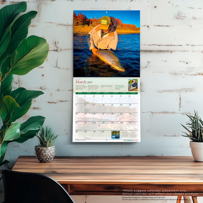 Puede incluir: Un calendario de pared para marzo de 2027 con una fotograf&iacute;a de una persona con chaqueta beige y gorra amarilla sosteniendo una trucha marr&oacute;n grande en un r&iacute;o. La cuadr&iacute;cula del calendario muestra las fechas del 1 al 31 con im&aacute;genes y texto.