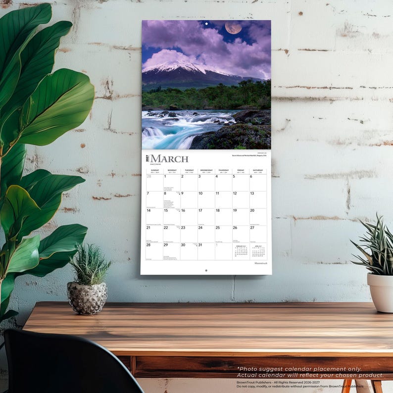 May include: A wall calendar for March 2027 featuring a landscape photograph of a snow-capped mountain peak under a purple sky with a moon, above a flowing river. The calendar grid displays the days of the month with the text March 2027 at the top.