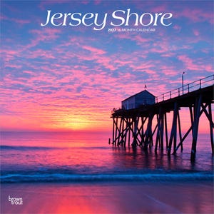 May include: A 2027 16-month calendar titled Jersey Shore featuring a photograph of a wooden pier extending over the ocean at sunrise. The sky is filled with vibrant pink and orange clouds above the calm water, with a small building on the pier.