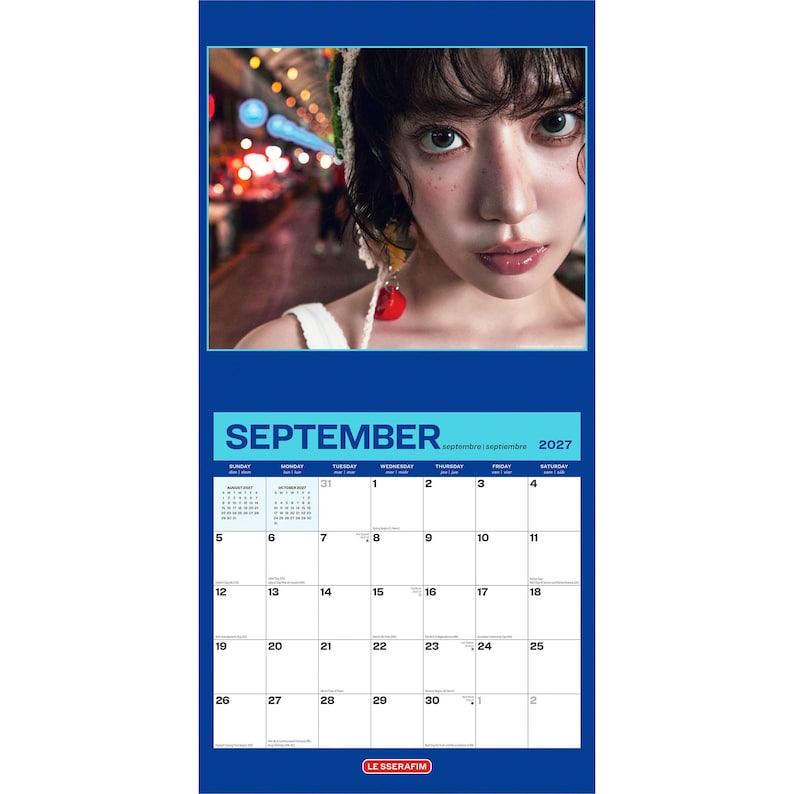May include: A wall calendar for September 2027 featuring a portrait of a person with dark hair and a white crocheted accessory. The calendar grid is printed in black on a white background with a blue border and the text LE SSERAFIM at the bottom.