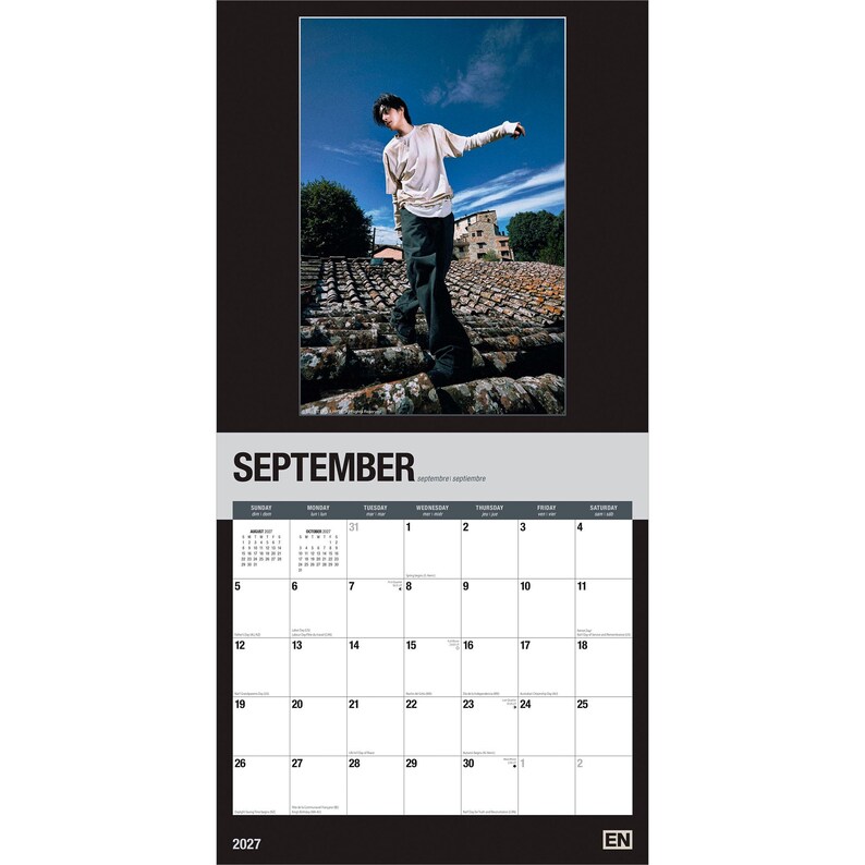 May include: A 2027 wall calendar for the month of September featuring a photograph of a person standing on a tiled roof against a blue sky. The calendar grid displays the days of the month with black text on a white background and the year 2027.