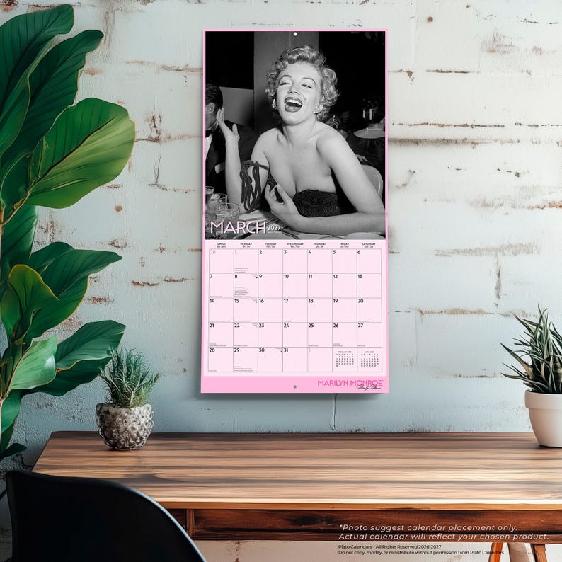 K&ouml;nnte beinhalten: Ein Wandkalender f&uuml;r M&auml;rz 2027 mit einem schwarz-wei&szlig;en Foto von Marilyn Monroe, die lacht. Der Kalender hat einen hellrosa Hintergrund mit einem Datumsraster, dem Text MARCH 2027 oben und MARILYN MONROE unten aufgedruckt.