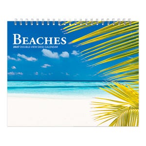 May include: A 2027 double-view desk calendar featuring a spiral-bound top and a scenic photograph of a white sand beach, turquoise ocean, and blue sky with clouds, partially obscured by bright yellow-green palm fronds on the right side.
